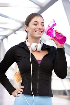 athletic woman with headphones smiling drinking water while exercising