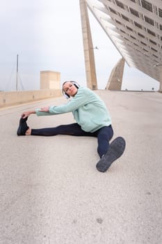 Sporty woman with sports headphones doing stretching sitting concentrated outdoors.