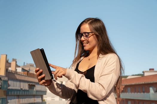 Beautiful young adult caucasian woman with glasses typing on tablet pc happy