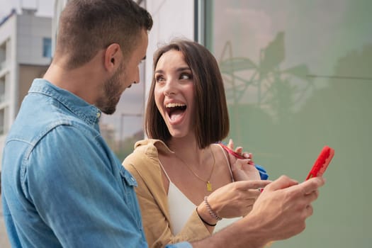 Pretty Caucasian couple of man and woman holding shopping bags, browsing smartphone apps buying online