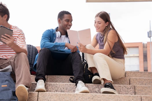 smiling multiracial college students sitting outdoors preparing for exam.