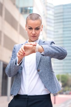 Caucasian businesswoman seriously looking at the time on the clock wearing a dress standing in an outdoor workspace. Front view of a young lawyer with thoughtful expression staring blankly