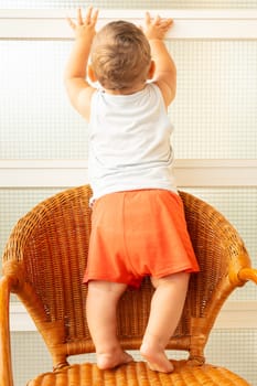 A baby climbs into a chair. A child in distress climbs onto furniture with the risk of falling. One-year-olds.