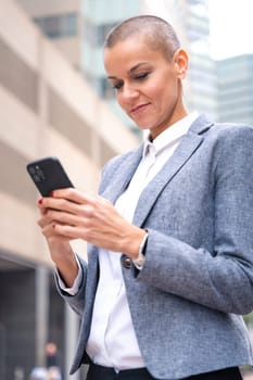 Satisfied with the results, the businesswoman walking on the street outside the office building, a mature boss holds a phone in her hands, writes messages and reads news online, using an app.
