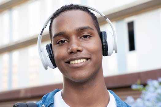 Young black man student standing outdoors at university with headphones.College life concept