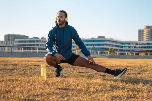 Young latin sportsman with sports headphones doing stretches with water bottle on the floor.