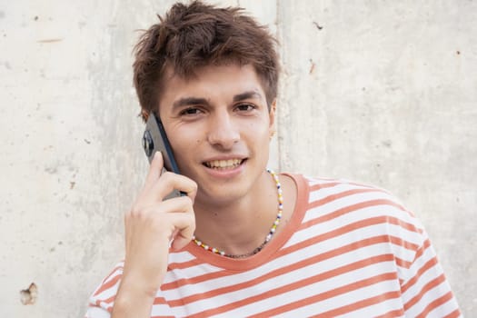 Beautiful caucasian teenage student smiling and talking on mobile phone outdoors. Boy talking on mobile phone