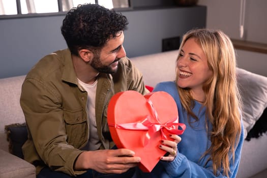 Young couple looking at each other lovingly with a surprise gift on their relationship anniversary. Loving and romantic date.