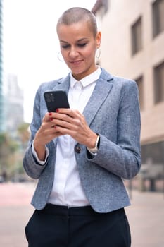 Satisfied with the results, the businesswoman walking on the street outside the office building, a mature boss holds a phone in her hands, writes messages and reads news online, using an app.