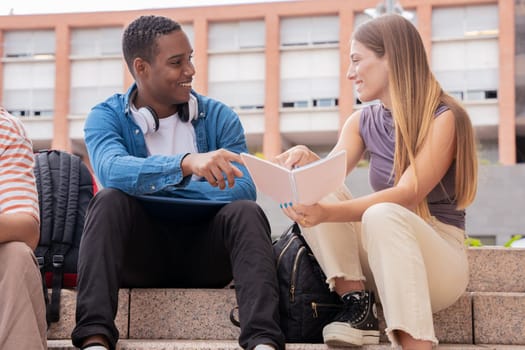 multiethnic smiling students sitting outdoors using a cell phone to chat online. University life concept