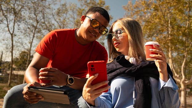 Happy multiracial couple in sunglasses making selfie on cell phone having fun an afternoon together in the park.