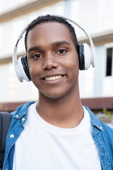 Young black man student standing outdoors at university with headphones.College life concept