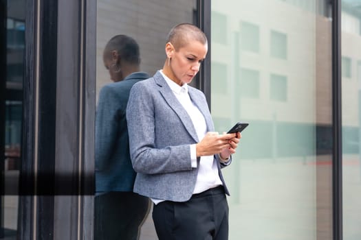 Satisfied with the results, the businesswoman walking on the street outside the office building, a mature boss holds a phone in her hands, writes messages and reads news online, using an app.