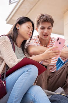 smiling multiracial students sitting outdoors using cell phone to chat online. University life concept