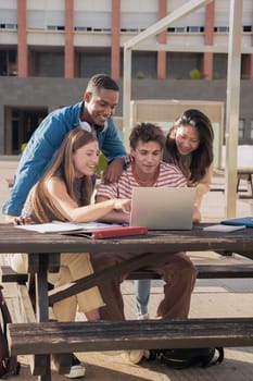 Vertical photo A group of four students with laptops and notes sit near the campus to review the exam.