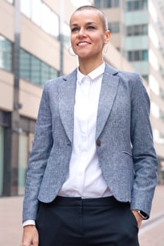 Caucasian businesswoman looking happy at the camera in a suit standing in outdoor workspace. Front view of a young lawyer with thoughtful expression staring
