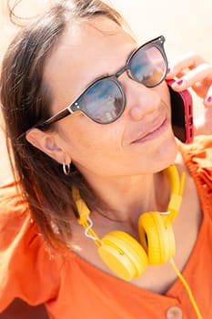 Close-up Beautiful young caucasian woman with headphones and sunglasses, having a conversation on cell phone.
