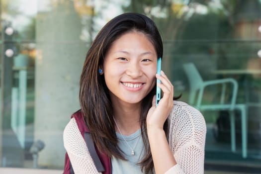 Beautiful Chinese teenage student smiling and talking on mobile phone outdoors. Girl talking on mobile phone