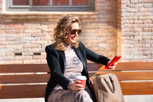 Woman wearing sunglasses with cell phone in hands, writes messages and reads news online, using an app.