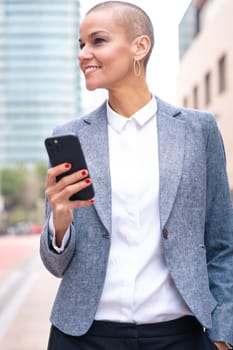 Satisfied with the results, the businesswoman walking on the street outside the office building, a mature boss holds a phone in her hands, writes messages and reads news online, using an app.