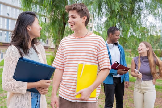 Happy university student friends talking and laughing while reviewing syllabus notes on campus. Diverse Asian and European youth