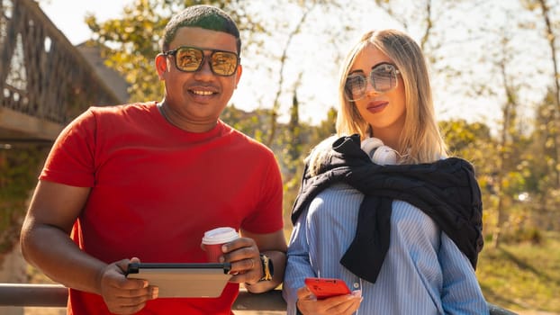 Cute multiethnic couple of man and woman standing browsing smartphone apps shopping online looking at camera