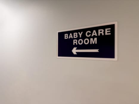 Sign on wall of corridor with directional arrow towards baby care room. Special room for parents to change the baby diaper. Important room when building infrastructure in public place