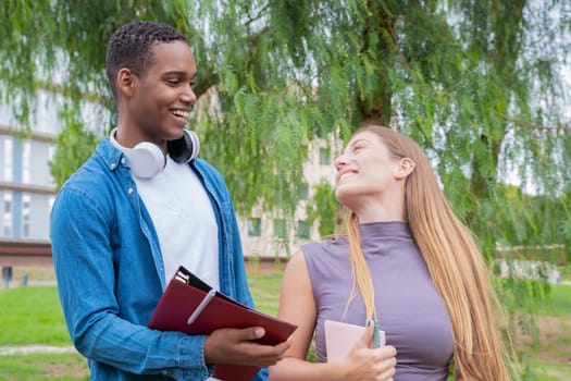 Happy college student friends talking and laughing while reviewing curriculum notes on campus. Diverse North American and European Youth