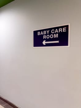 Sign on wall of baby care room and an arrow indicating direction along corridor. Help with orientation in public places. Baby care room right next to hall, vertical photography