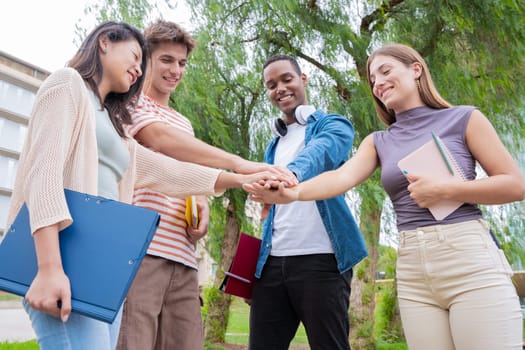 Multiracial group of students with notebooks in hand joining hands on campus. having fun supporting each other.