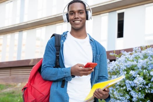 A happy student with headphones and folder is inside the university campus using a social media application. College life