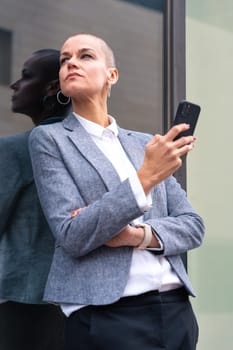 Satisfied with the results, the businesswoman walking on the street outside the office building, a mature boss holds a phone in her hands, writes messages and reads news online, using an app.