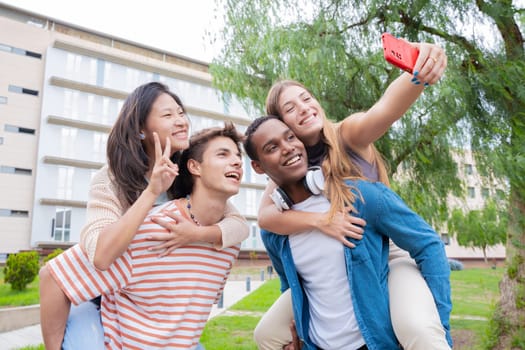 Young students piggybacking their fellow college students on campus. Excited friends posing for a funny photo.