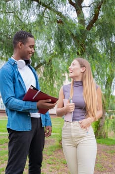 Happy college student friends talking and laughing while reviewing curriculum notes on campus. Diverse North American and European Youth