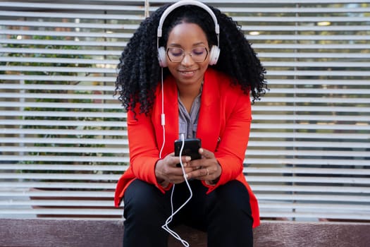 Beautiful black woman smiling using a social media app on a mobile phone outdoors. Girl chatting on mobile phone
