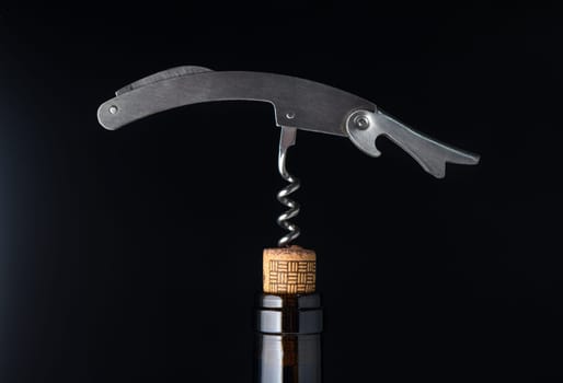 A sleek corkscrew stands ready above a wine bottle, highlighting its modern design against a dark background.