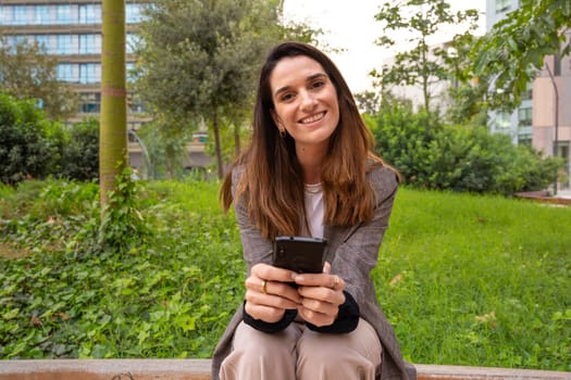 Young Woman with cell phone in hands, writes messages and reads news online, using an app looking at camera.
