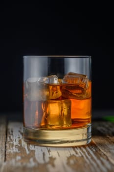 A glass filled with a golden drink and ice sits on a rustic wooden table, glistening under soft light.