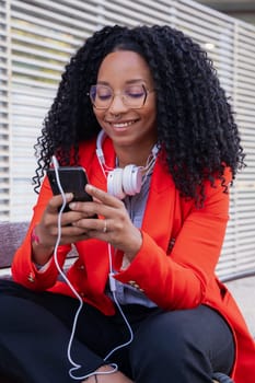 Vertical shot Beautiful black woman smiling using a social media app on a mobile phone outdoors. Girl chatting on mobile phone