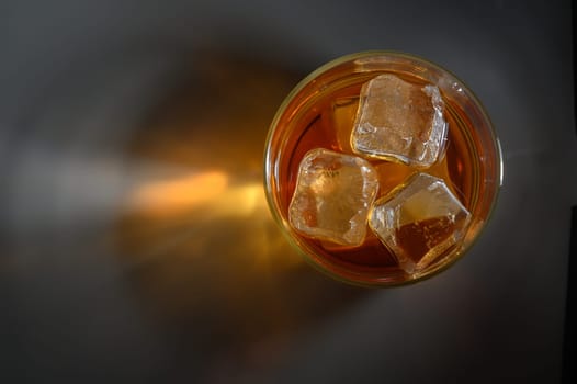 A clear glass filled with iced tea and ice cubes sits on a dark surface, evoking a serene summer vibe.