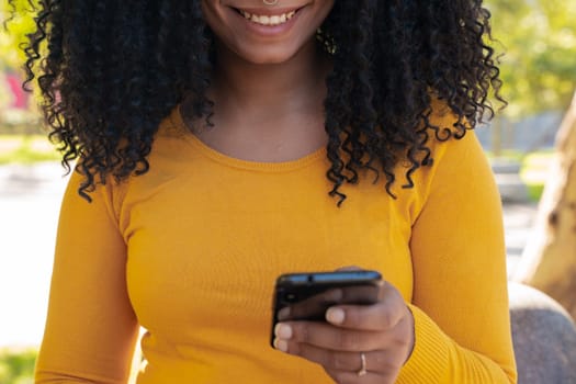 close-up of a beautiful black woman smiling while holding, using and looking at a smartphone with a feeling of happiness