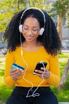 vertical photo happy black woman with credit card and smartphone in hands. Concept: online shopping