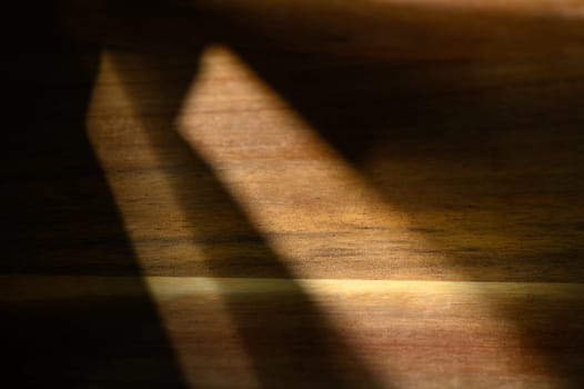 Soft rays of afternoon light gently illuminate a wooden surface, casting delicate shadows that enhance its texture.
