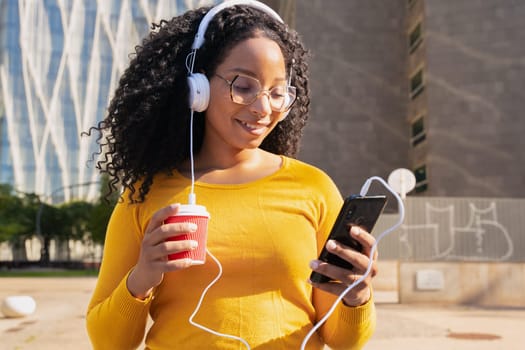 Happy teenager with headphones,drinking coffee sending messages using a cell phone outdoors. Communication