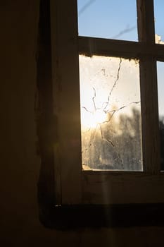 Golden rays illuminate the interior as sunlight streams through a shattered window, revealing a sense of nostalgia.