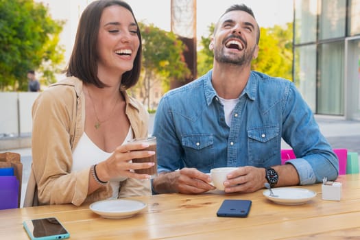 Two young friends chatting on a cafeteria terrace drinking coffee, laughing and having a good time after work.
