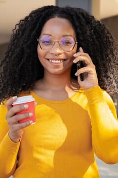 Vertical photography Young smiling black student talking on mobile phone while drinking coffee on university campus. Concept: university life