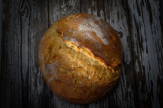 A perfectly baked round loaf showcases its golden crust and inviting aroma on a weathered wooden table.