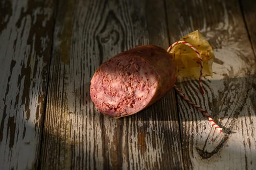 Savory delicacy wrapped in yellow paper sits on a textured wooden surface under gentle sunlight, enhancing its features.
