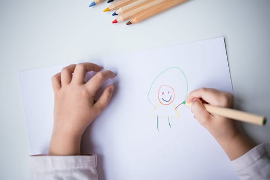 Child drawing colorful smiley figure with pencils on white paper.